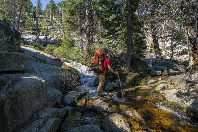 Backpacker crossing a rocky stream on the way to Bearpaw Meadow