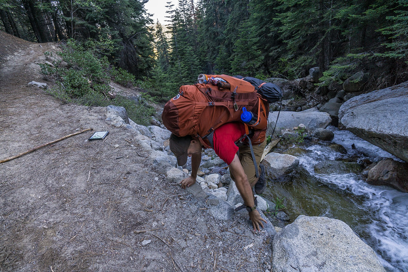 Backpacker climbing the steep bank after a stream crossing