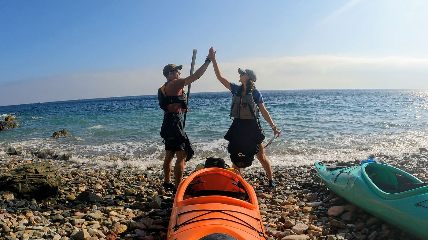 high-five-pakayak.jpg Two kayakers high-five beside their orange and teal Pakayaks on the beach