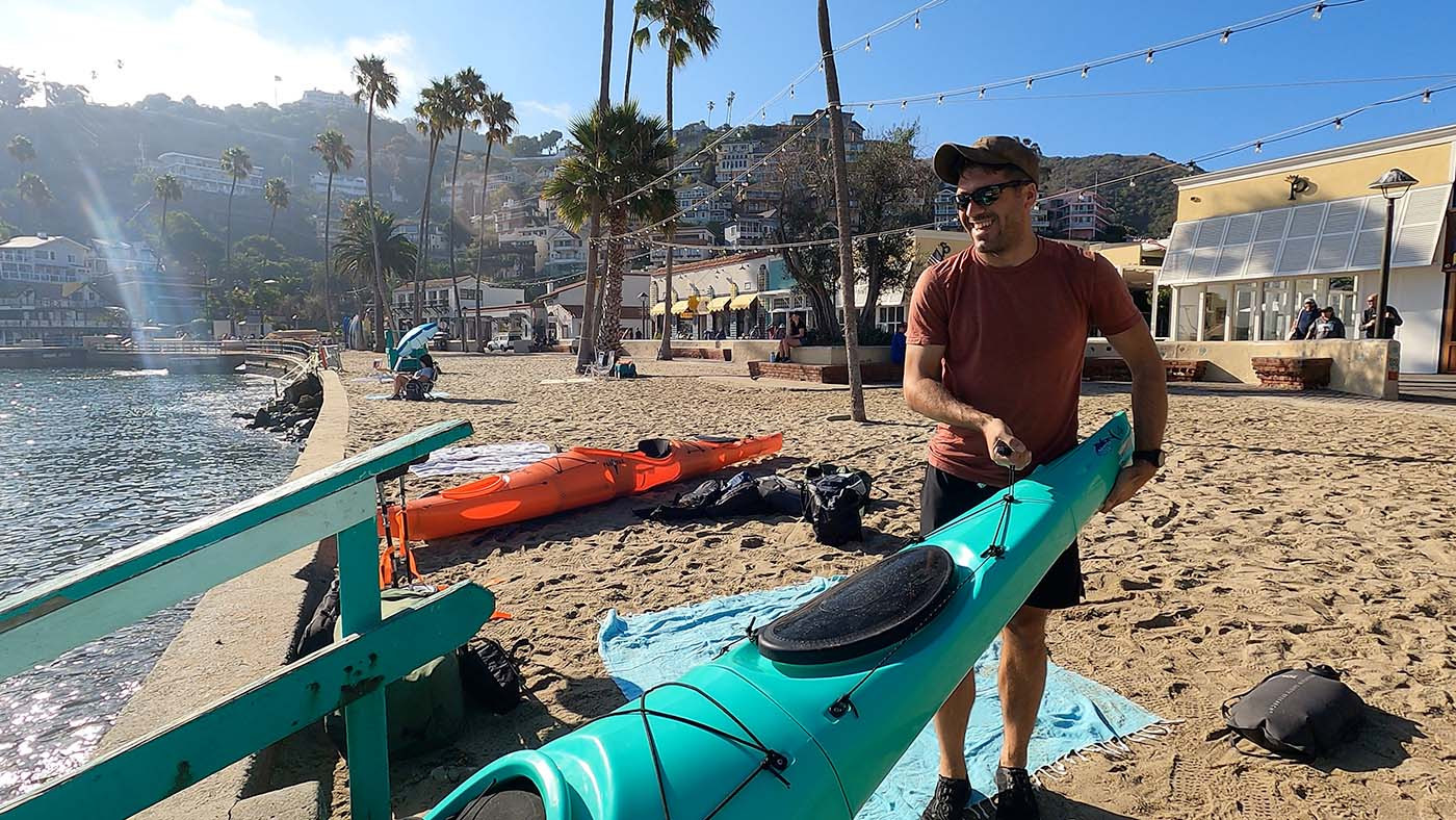 carry-pakayak-to-beach.jpg Kayaker carrying an assembled teal Pakayak toward the water in Avalon