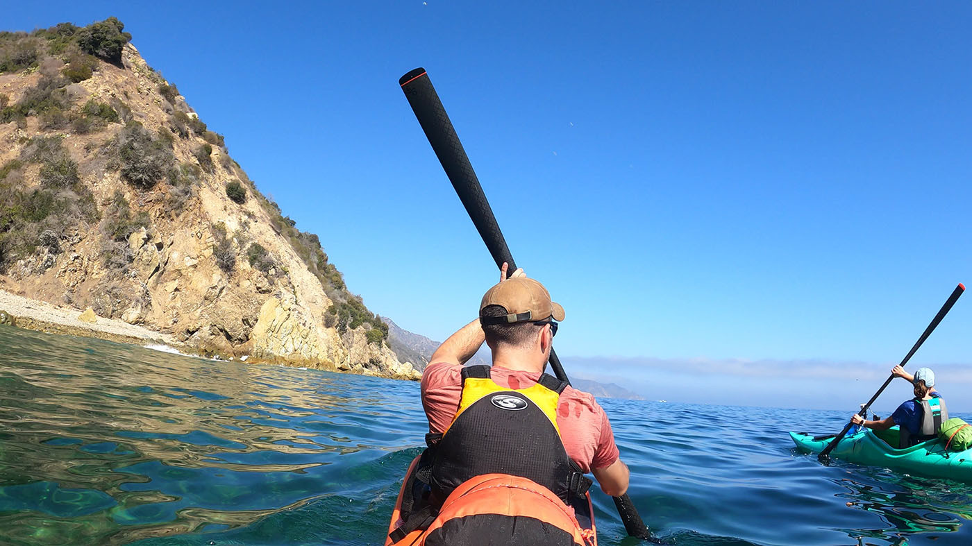 day-1-easy-kayaking.jpg Two kayakers paddling calm blue water beneath Catalina Island cliffs